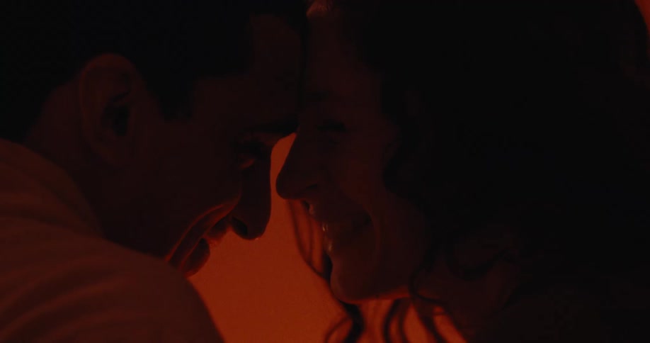 Man and a woman rest their foreheads against each other in a room lit by soft orange light