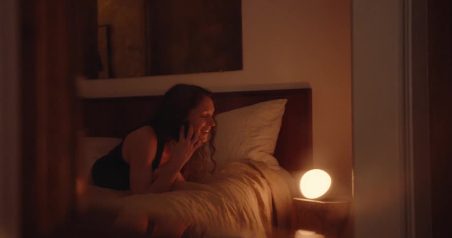 A woman lies on her bed while talking on her smartphone
