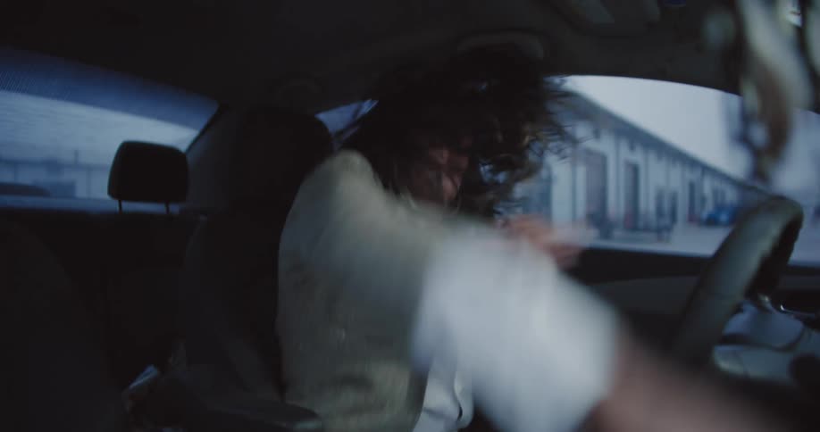 Man drums with his hands and feet while head banging in a parked car