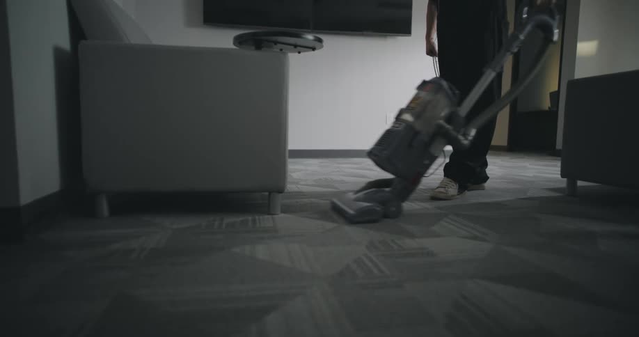 Woman vacuums the carpet in the living room during the day