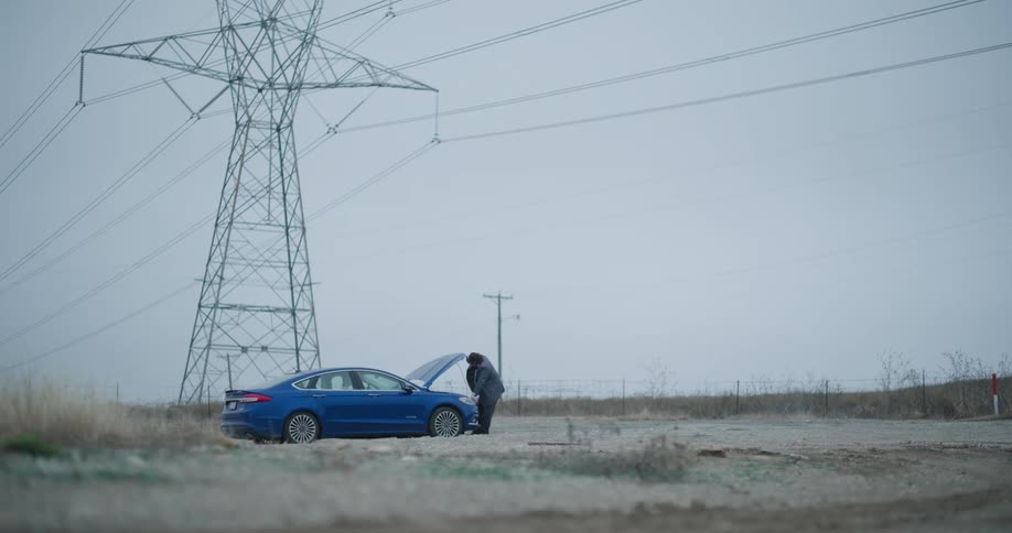 Man becomes upset after examining his car which has broken down in the rural countryside near a transmission tower