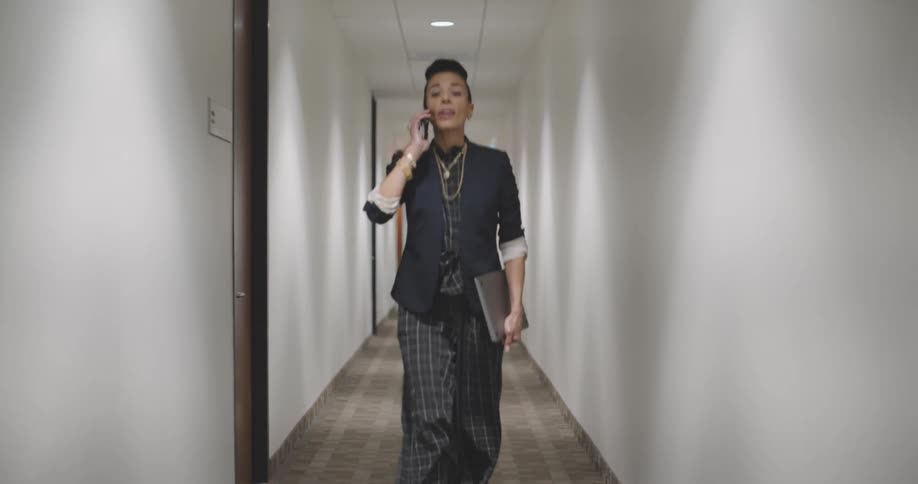A woman talks on her phone while walking down the hallway