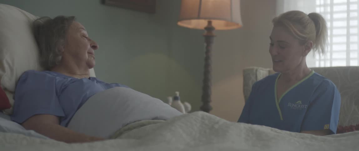 A nurse attends an older lady in bed