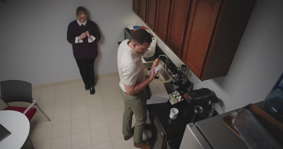 Man closing the refrigerator and taking a sweet bread from a box and next to him a woman taking a lunch box from a microwave