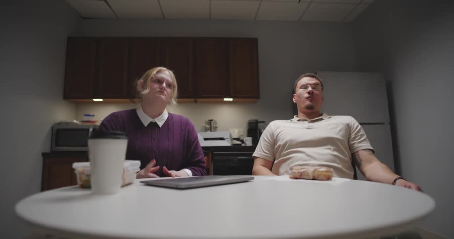 Woman closing her laptop while sitting next to a man who is eating a sweet bun