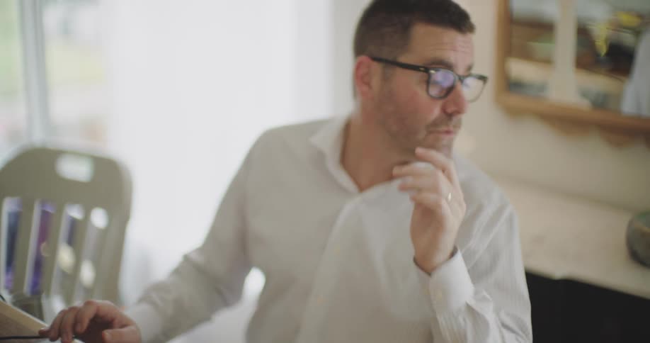 Father sitting at the table working in front of the laptop and interacting at the same time with his little son next to him