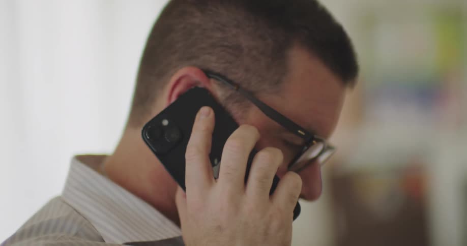 Close up of a man talking on a smartphone with a blurred room in the background
