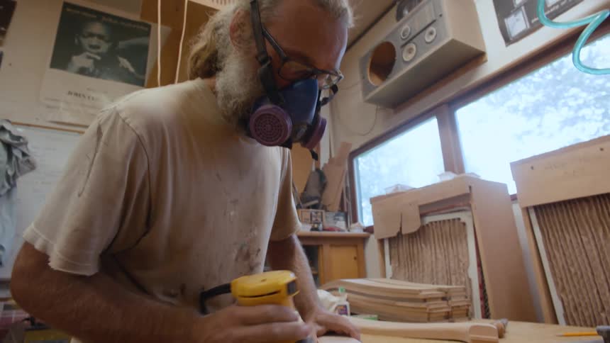 A man in a mask is using a tool to scrape the surface of a wooden object