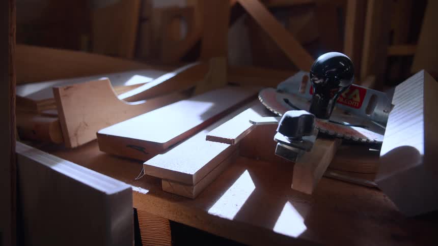 A woodworking workbench with a circular saw various pieces of wood and a clamp all illuminated by natural light