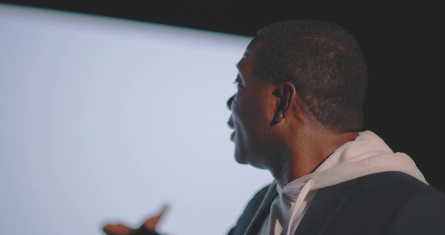 Portrait of a man lecturing and pointing at a screen