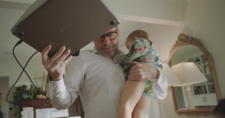 Father standing holding a laptop and holding his little son with children around