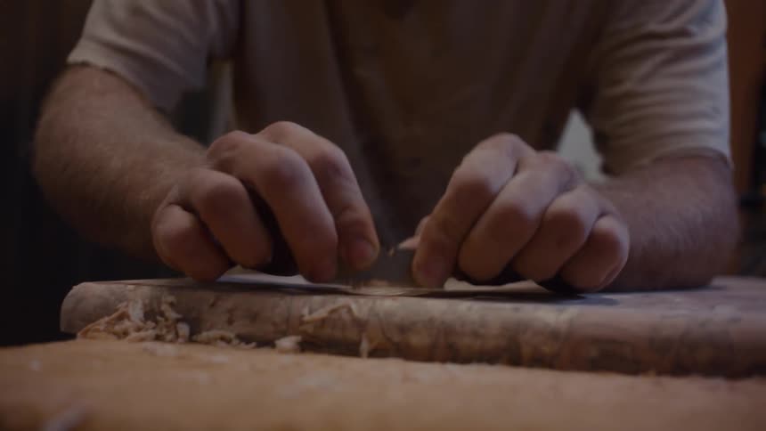 Carpenter with protective mask scraping a piece of wood