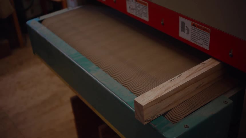 Hand places pieces of wood on an industrial sander