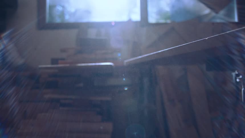 A sunlit workshop interior is seen through a window and a partially obscured wooden plank