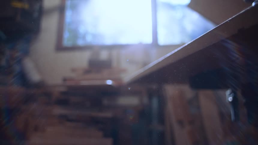 A sunlit workshop interior is seen through a window and a partially obscured wooden plank