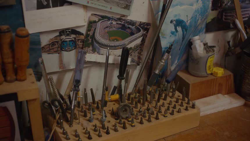 A cluttered workbench displays an array of tools and a stadium picture amongst a collection of items