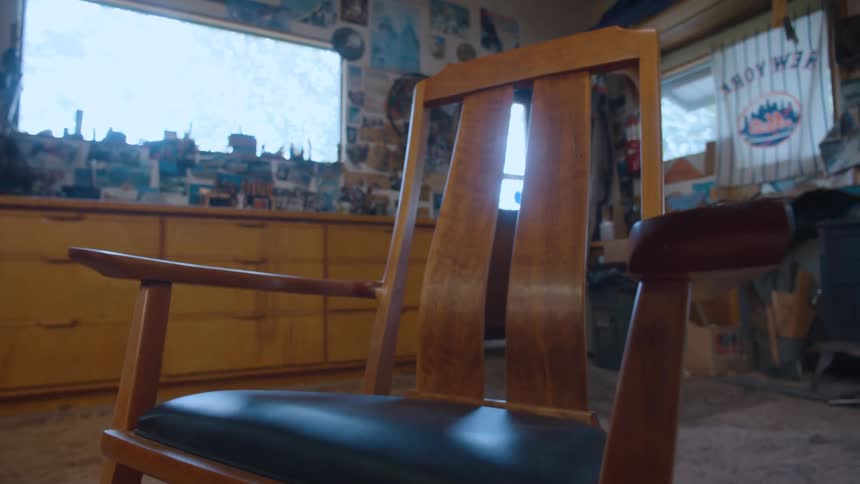 A midcentury modern rocking chair with a dark blue seat faces a sunlit window in a cluttered workshop