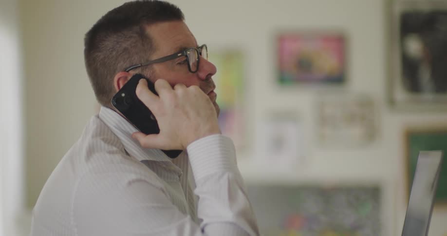 A parent working from home talks on a smartphone with a wall of childrens artwork in the background