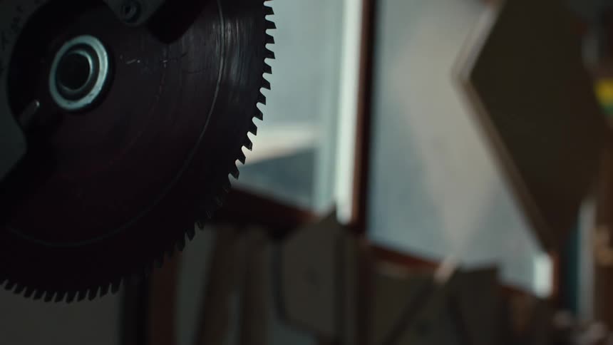 A circular saw blade with sharp teeth is positioned against a backdrop of a brightly lit window and a cluttered workshop