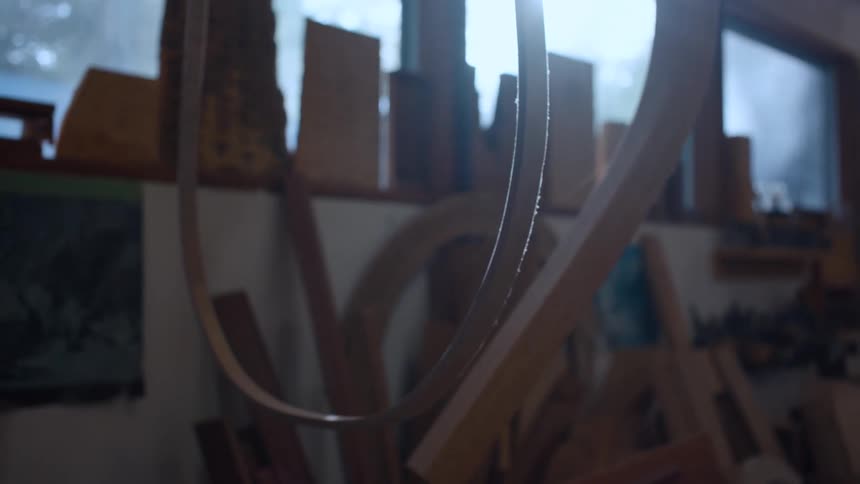 A brightly lit window casts light into a cluttered workshop revealing various woodworking tools and materials
