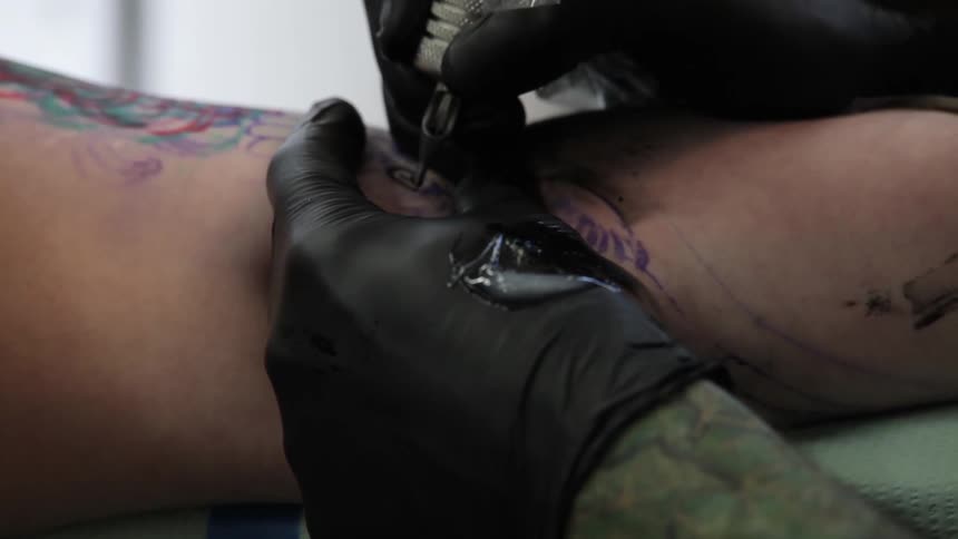 Limb being tattooed by gloved hands