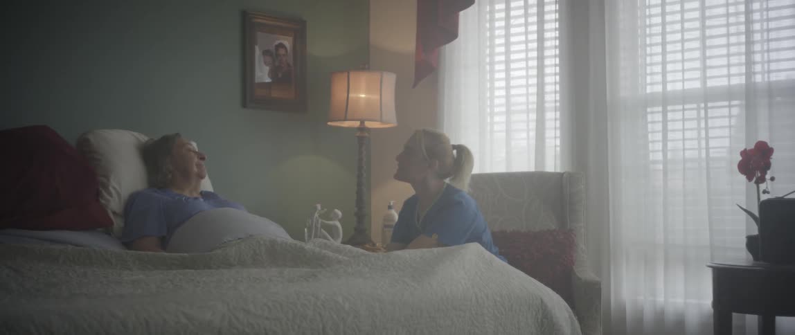 A nurse gives an elderly woman a sip of water and sits down