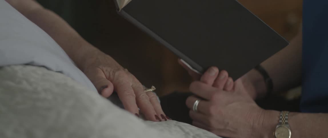 Person reads to an elderly person laying in bed