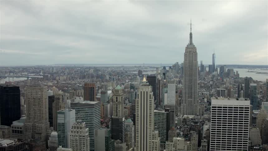 The empire state building standing amongst other large buildings on a cloudy day