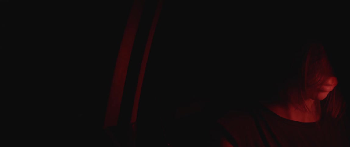 A red light illuminates a woman's neck in a very dark area