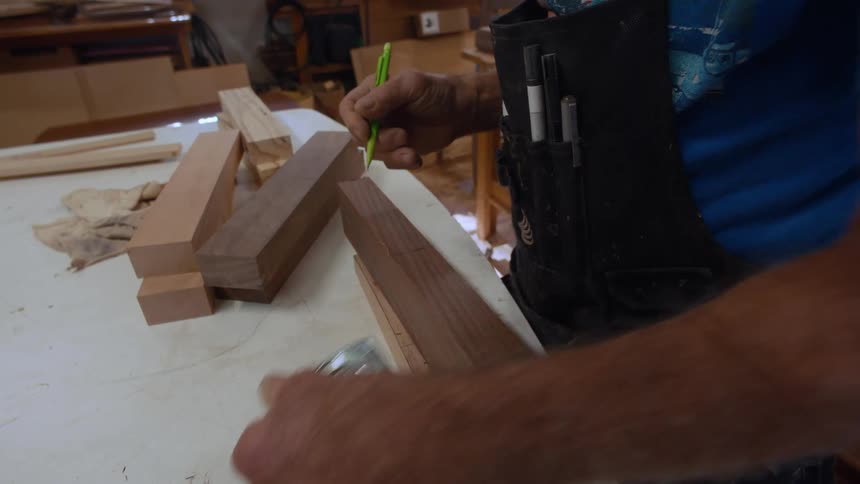Carpenter with a pencil and a tape measure measuring a piece of wood on a table