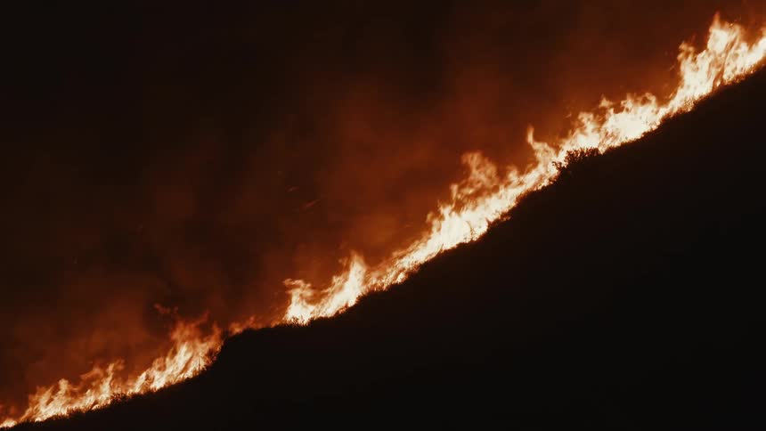Silhouette of a mountain with vegetation on fire at night