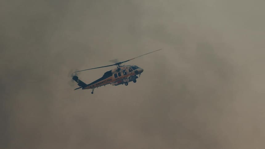 A blue and white helicopter flying below the clouds