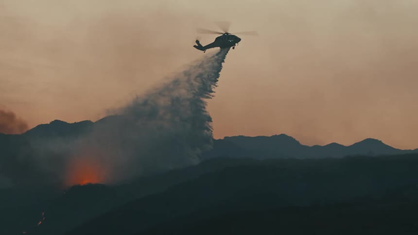 Helicopter dropping water on a wildfire in the mountains