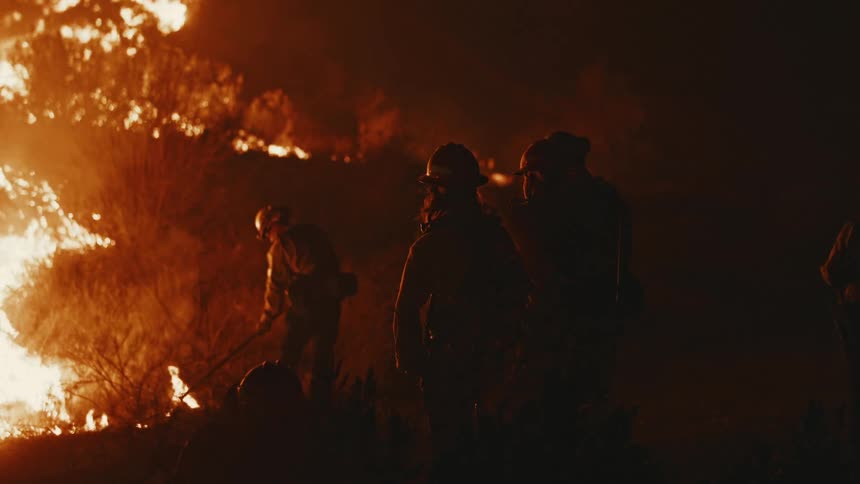 A group of firefighters smothering a wildfire in the hills at night