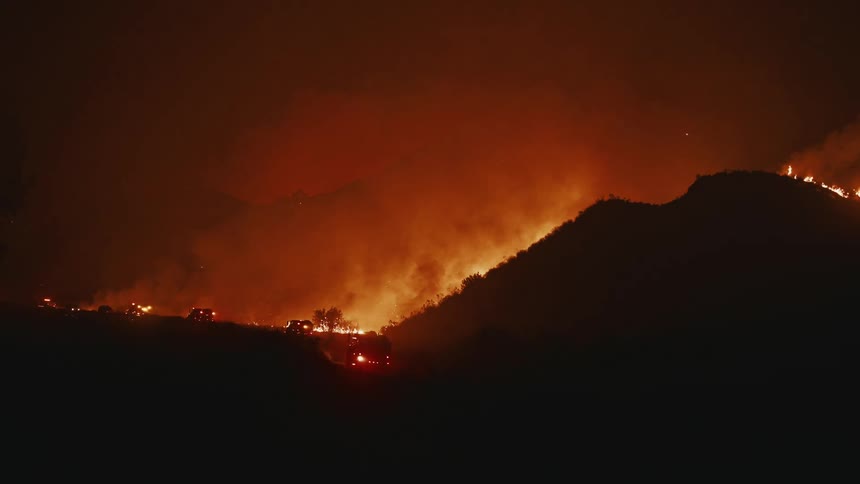 A devastating wildfire burning across a dark landscape with bright orange flames illuminating the scene