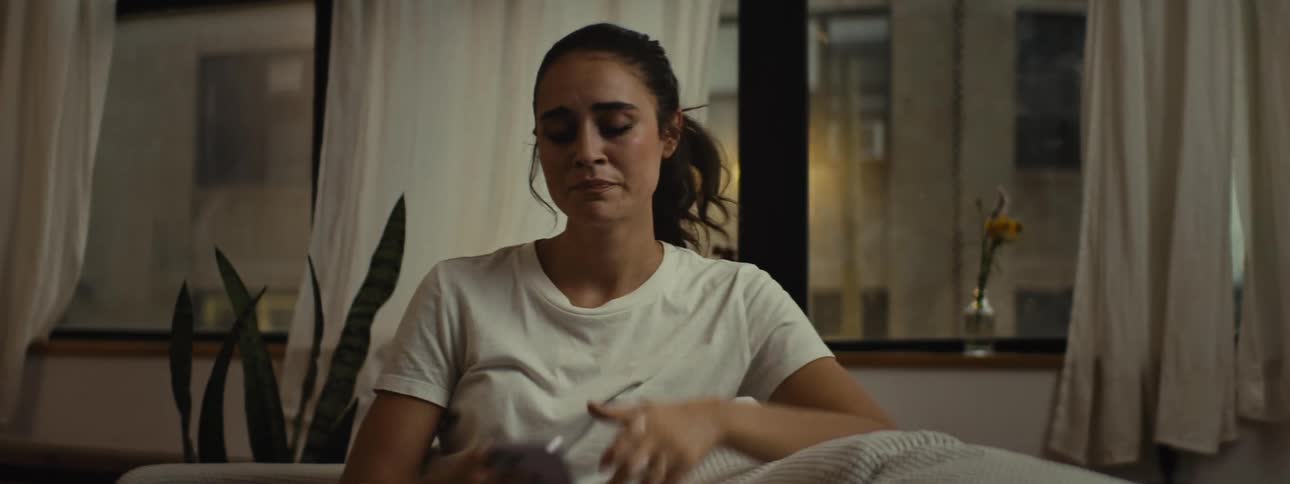 A sad woman sits on the couch at home texting on a smartphone while crying