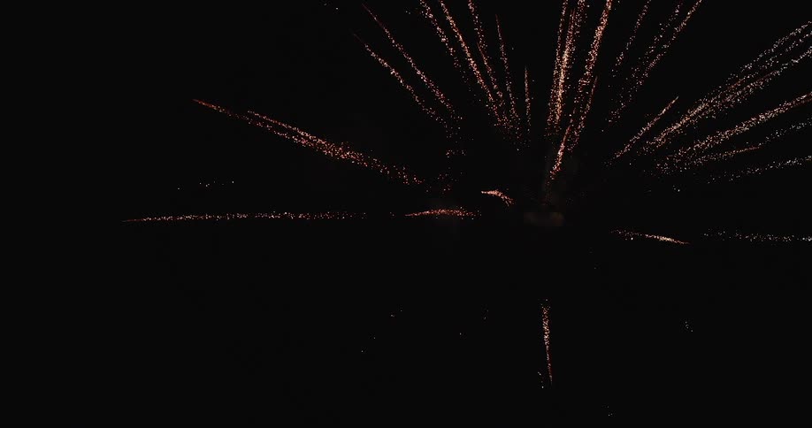 Multiple fireworks explode overhead lighting up the night sky with bright sparks and comet trails
