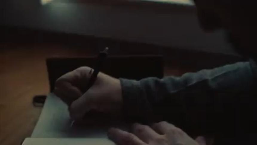 A person is writing with a pen on a piece of paper in a dimly lit room