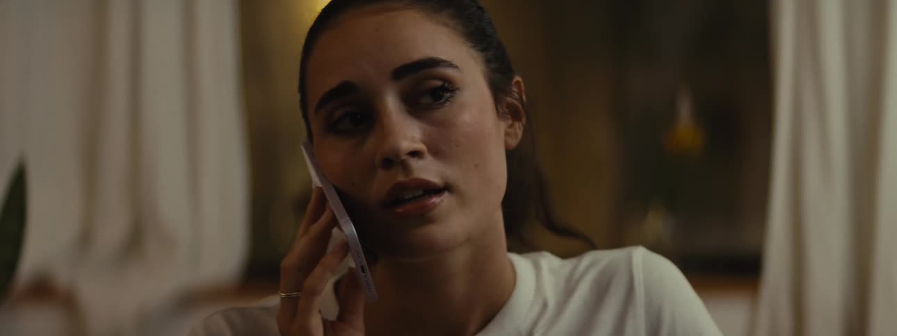 The face of a young woman who has her phone to her ear and is talking while looking to the sides and forward