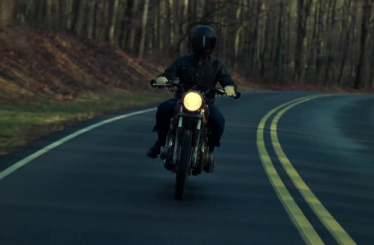 Person in helmet on a motorcycle traveling along a road surrounded by trees