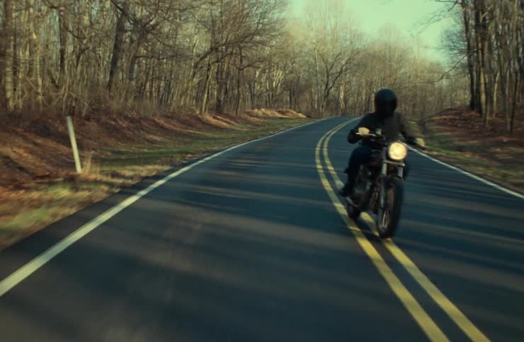 Motorcyclist rides a motorcycle along a highway past a forest of leafless trees