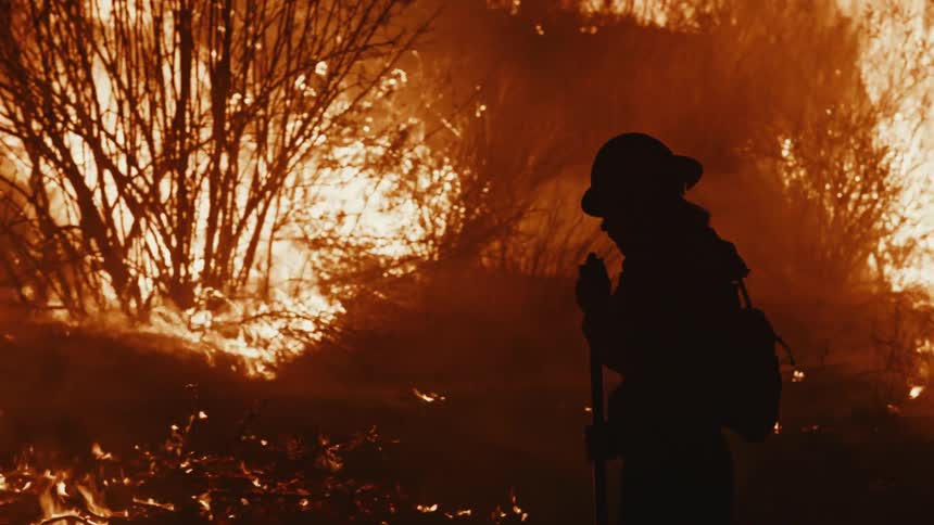 Silhouette of a firefighter walking in a forest with an active fire at night