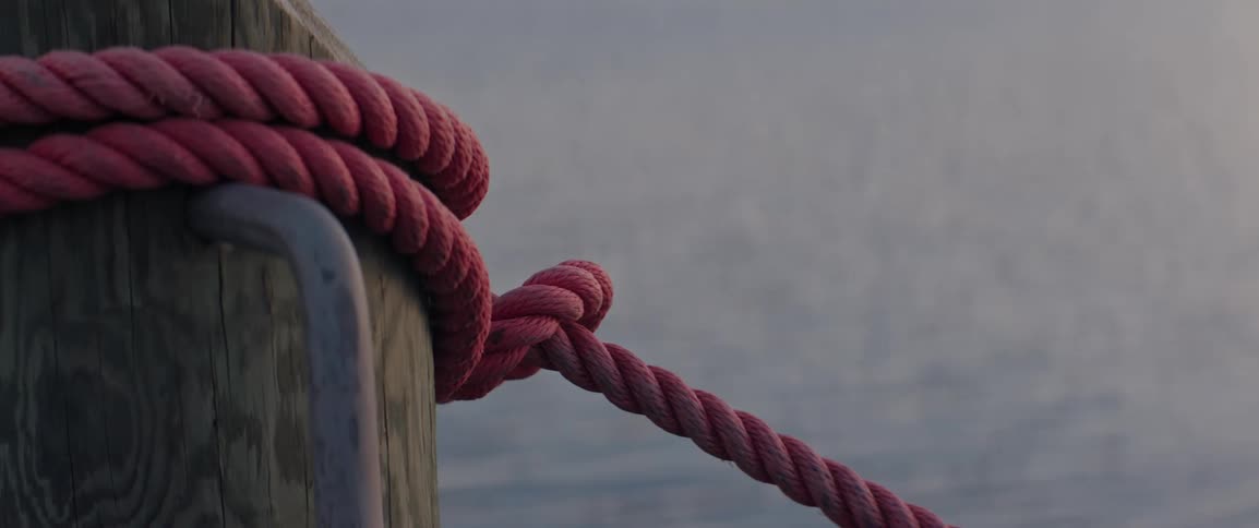 A red marine rope is secured around a dock post beside gently rippling water
