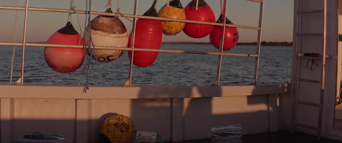 A persons shadow pushes a crab trap across the deck of a fishing boat at sunset