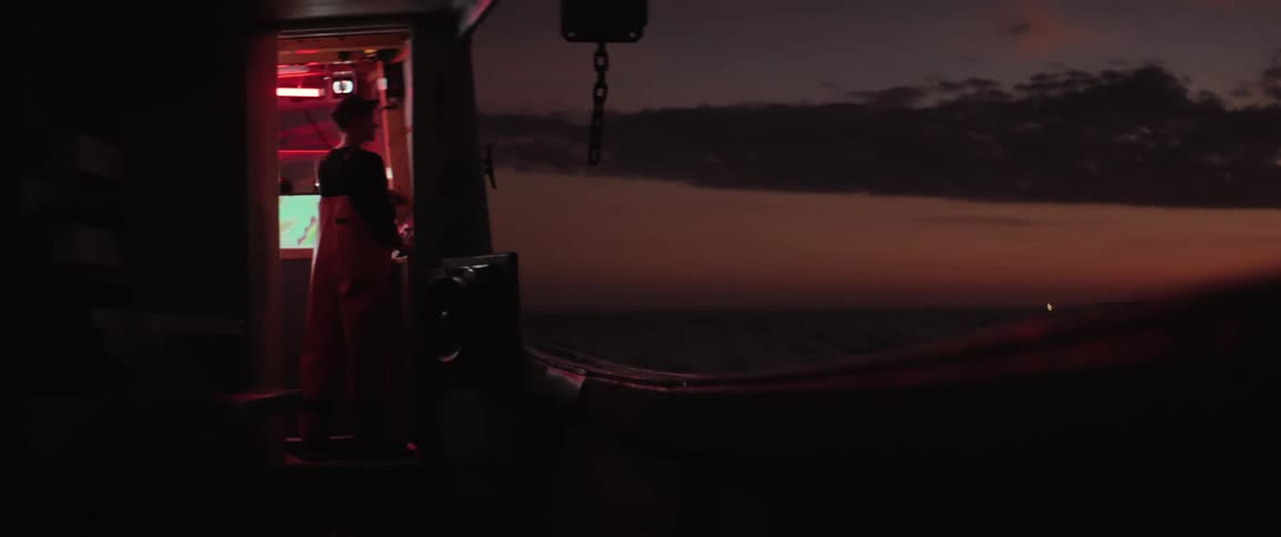Silhouette of a person in the cabin of a boat moving through the sea at night