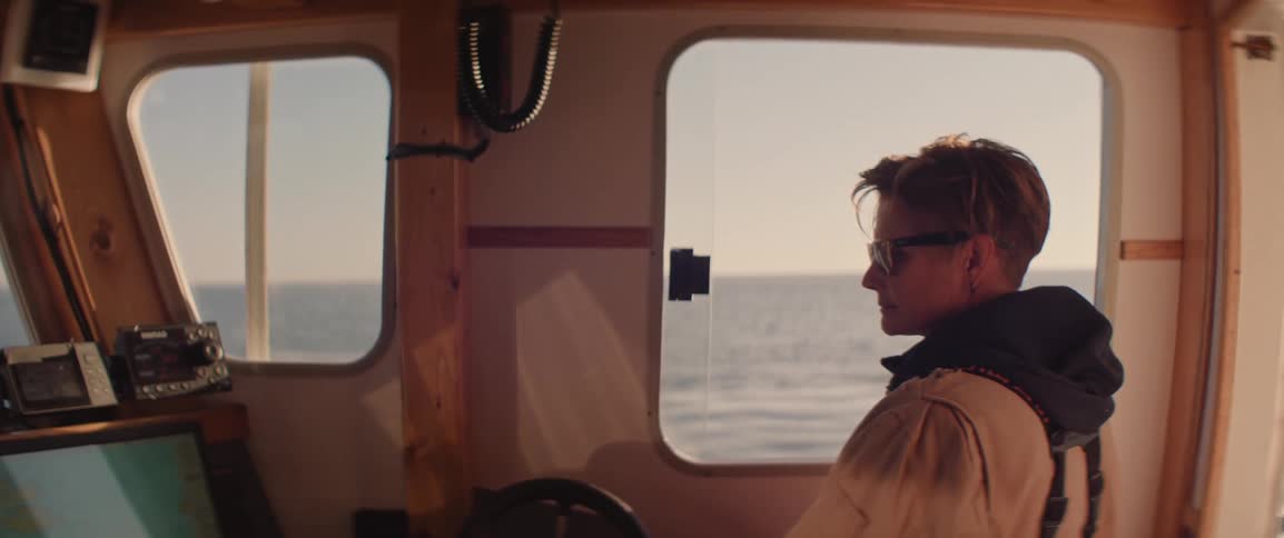 Woman in the cabin of a boat looking out the window at the ocean in the morning