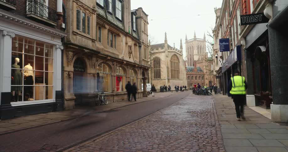 Cobblestone street surrounded by historic buildings and shops has pedestrians walking by