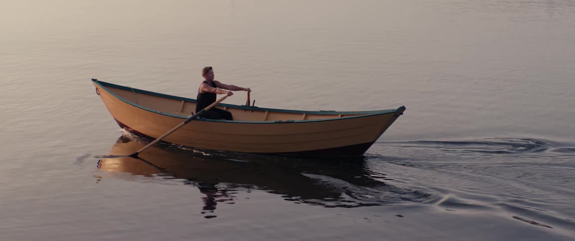 Person rowing a wooden boat in calm waters during sunrise