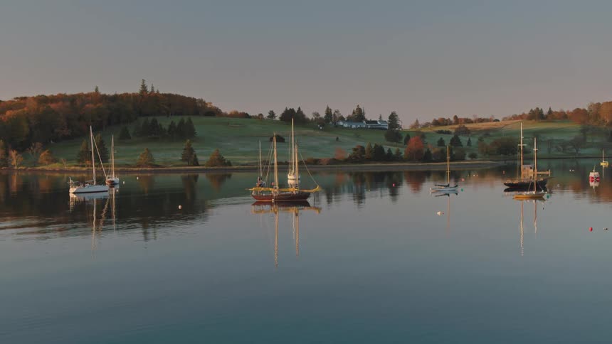 Calm bay with several sailboats and rolling hills in the background