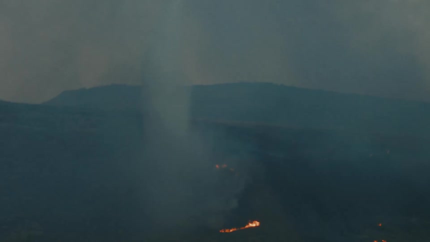 A helicopter hovers above a patch of burning ground dropping water onto the flames below